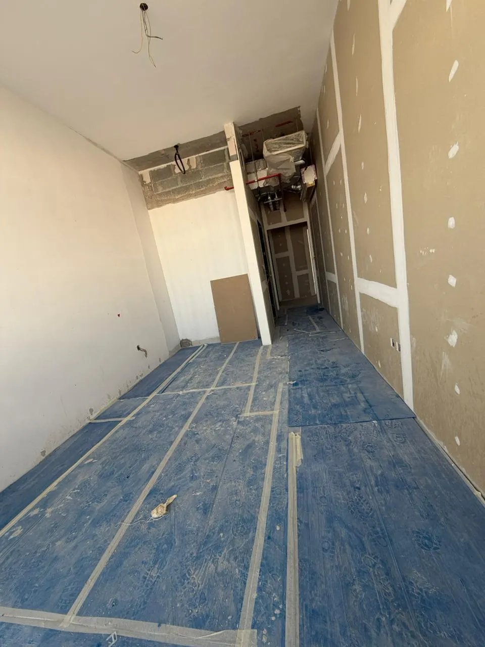 Corridor with partition walls built and protective sheeting taped over the finished floor