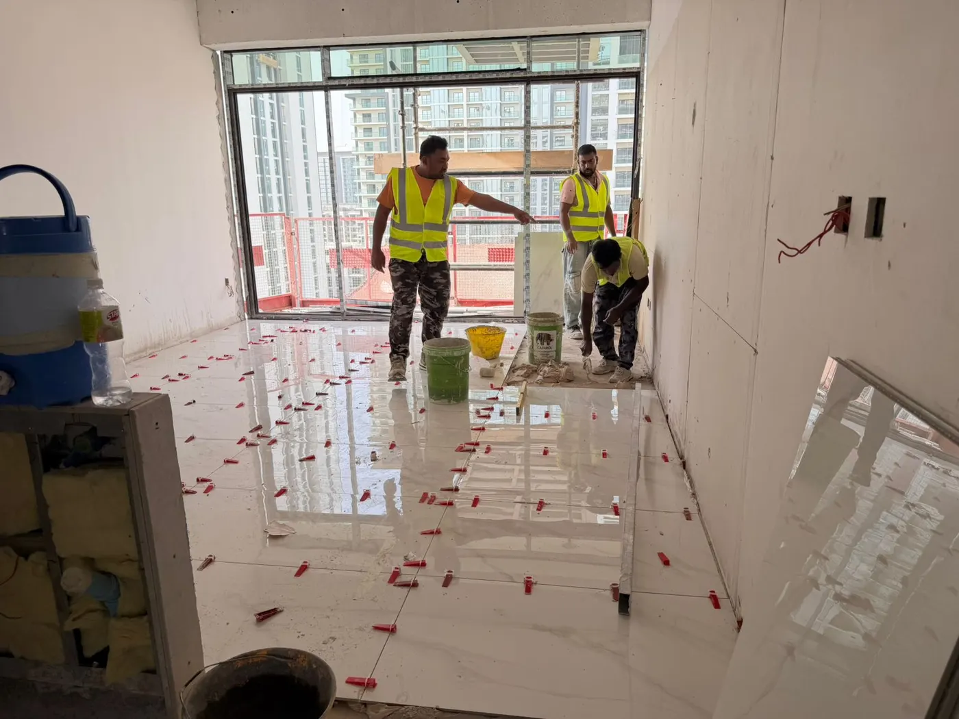 Technicians laying large-format floor tiles across a bare apartment living area
