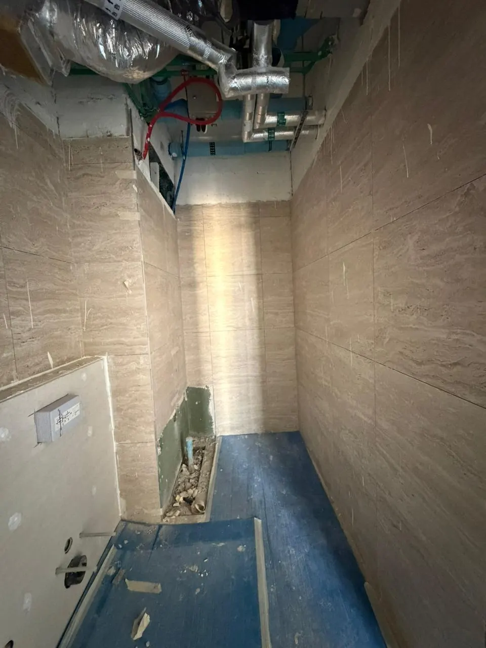 Overhead ductwork and pipework run above a tiled wet area before the ceiling closes